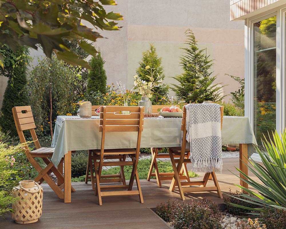 Lantern next to wooden chairs and table on the terrace of house with plants and blanket - Pam Duffel